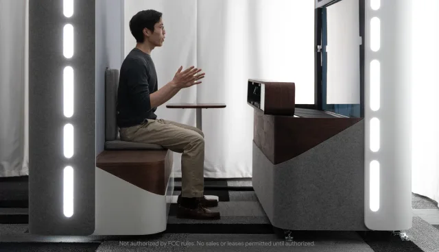 A seated participant using the original Project Starline booth, with its large display and surrounding capture equipment.