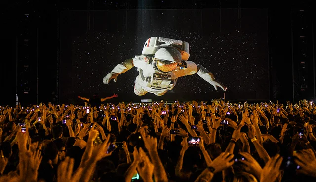 A crowd facing a stage with a large projected astronaut above the performers.