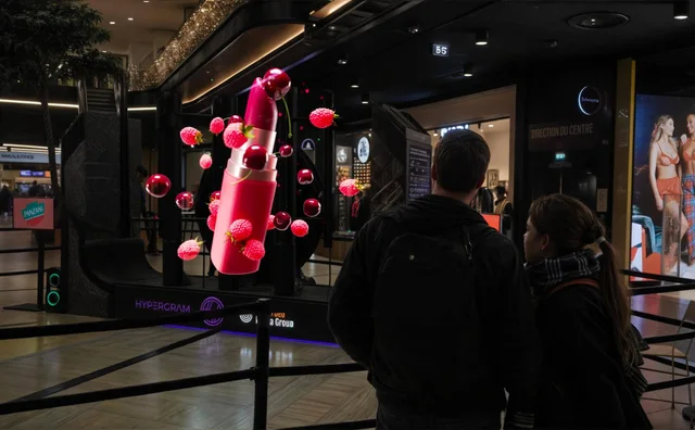 Visitors looking at a large floating lipstick visual in a shopping-centre HYPERVSN installation.