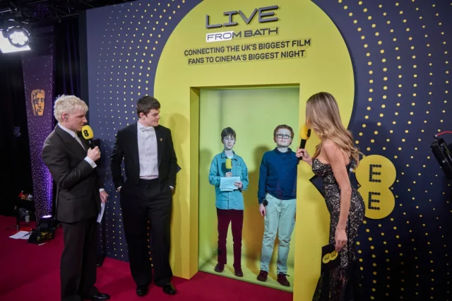 An EE and BAFTA branded event scene with two remote participants shown in a yellow portal beside presenters.
